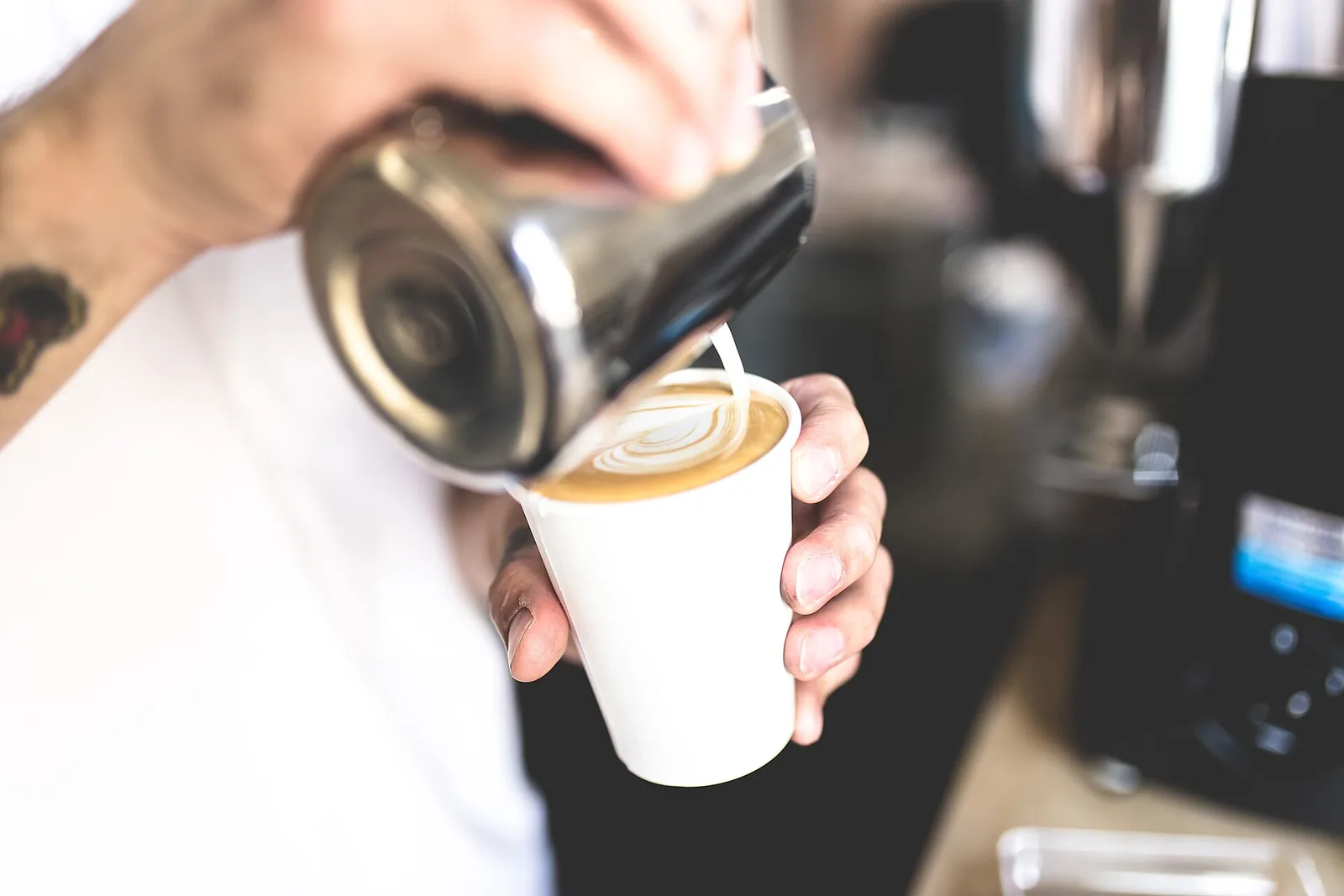 A barista pouring steamed milk into a cup